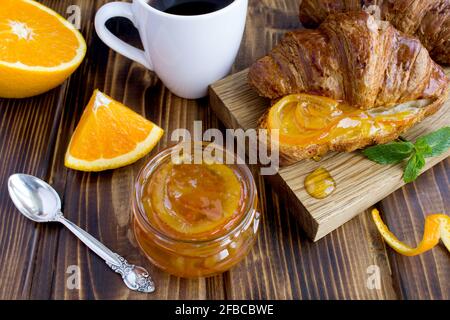 Marmellata d'arancia fatta in casa nel bicchiere, croissant e caffè lo sfondo di legno marrone Foto Stock