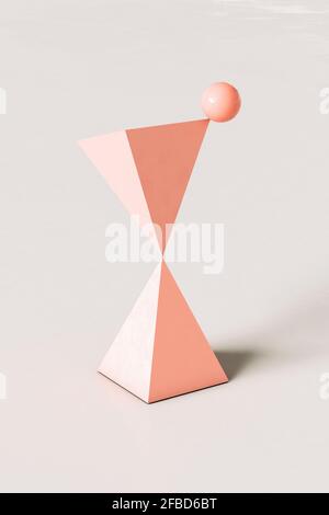 Piramidi astratte rosa con una sfera che si bilancia in cima sfondo color crema Foto Stock