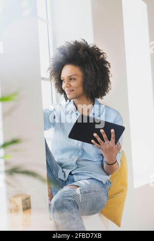 Giovane donna con tablet digitale seduto alla finestra Foto Stock
