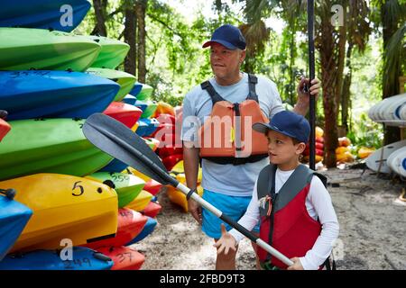 Figlio con ruggito che guarda la canoa mentre si trova in piedi da padre Foto Stock
