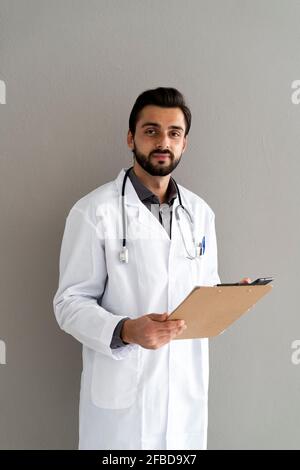 Bel medico maschile con appunti in piedi di fronte al muro Foto Stock