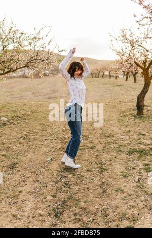 Donna spensierata che danzano con la mano sollevata agli alberi di mandorle Foto Stock