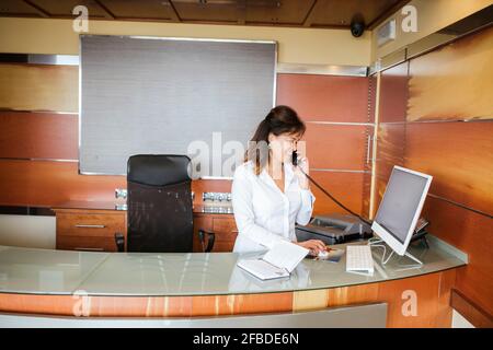 La receptionist femminile sorride e parla al telefono alla reception Foto Stock