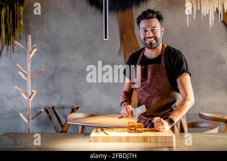 Chef sorridente con carne sfaldante in piedi da cibo in commercio cucina Foto Stock