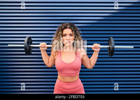 Giovane atleta in piedi con il barbell davanti al blu parete Foto Stock