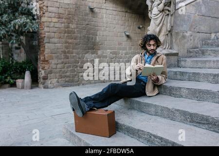 Giovane uomo con i piedi su leggere libro mentre si siede sopra fasi Foto Stock