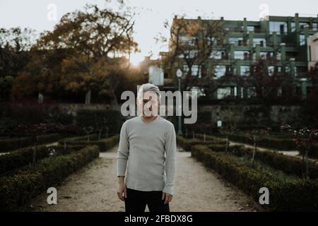Uomo dai capelli grigi seduto su radici di albero in giardino Foto Stock