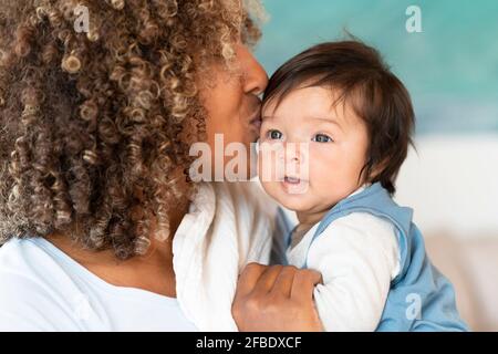 Madre che baciano il bambino carino sulla fronte a casa Foto Stock