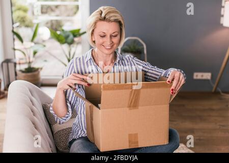Donna sorridente matura che apre la scatola a casa Foto Stock