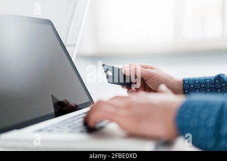 Mano di imprenditore maschile utilizzando il computer portatile mentre si tiene la carta di credito in ufficio Foto Stock
