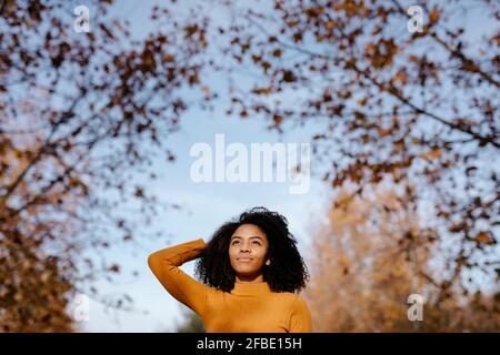 Donna afro pensierosa con testa in mano in piedi nel parco durante l'autunno Foto Stock