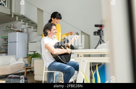 Coppia allegra che suona la chitarra mentre vlogging a casa Foto Stock