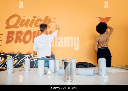 Giovane coppia multietnica pittura con spruzzare lattine su muro in studio Foto Stock