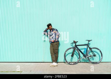 Bell'uomo con bicicletta appoggiato da una parete turchese sul sole giorno Foto Stock