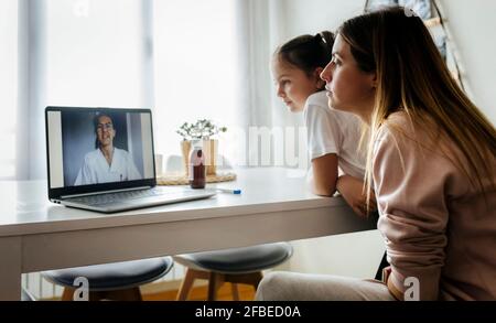 Ragazza e donna che ascoltano la pediatra femminile in videochiamata tramite un computer portatile a casa Foto Stock