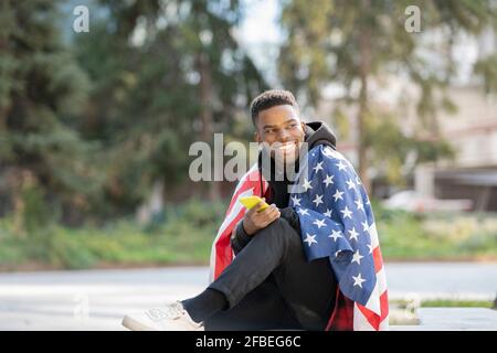 Giovane uomo avvolto in bandiera americana mentre si guarda via parcheggio Foto Stock