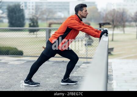 L'uomo atletico appoggiandosi sulla recinzione chainlink mentre fa l'esercitazione di stiramento al parco Foto Stock