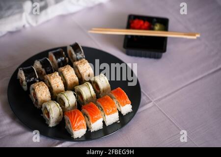 Un piatto con un set di sushi si erge su un copriletto bianco, rotola per una cena romantica. Cucina tradizionale giapponese Foto Stock