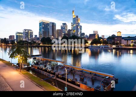 Germania, Assia, Francoforte, Tourboat ormeggiato sulla riva del meno al tramonto con skyline di Mainhattan sullo sfondo Foto Stock