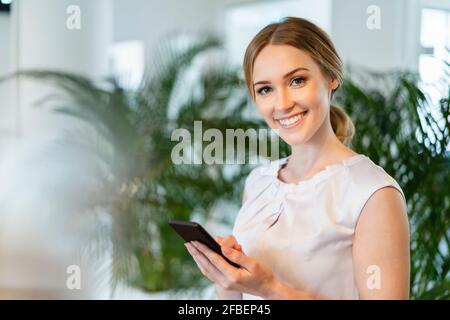 Sorridente bella imprenditore femminile in possesso di smartphone in ufficio Foto Stock