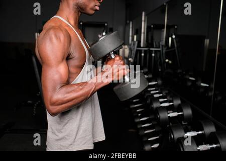 Atletico giovane maschio che si esercita con manubri in palestra Foto Stock