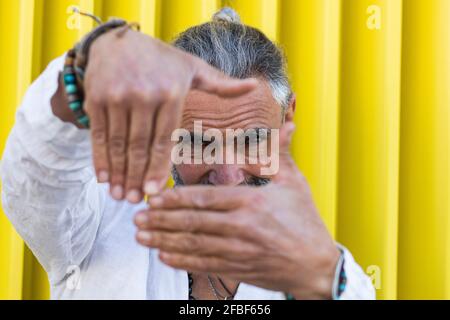 Uomo con capelli grigi che fanno la cornice del dito di fronte parete Foto Stock