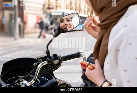 Giovane donna che applica il rossetto mentre guarda nello specchio del motociclo Foto Stock