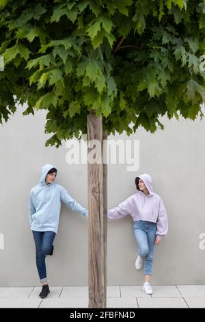 Coppia adolescente che si guarda l'un l'altro tenendo le mani per albero appoggiandosi alla parete Foto Stock