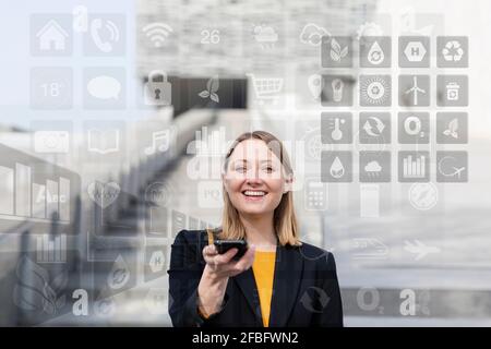 Donna d'affari sorridente che tiene il telefono cellulare con diverse icone intorno all'esterno Foto Stock