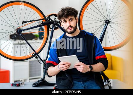 Uomo che tiene un tablet digitale in bicicletta a casa Foto Stock