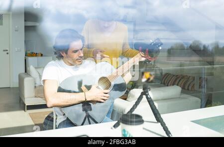 Donna che discute con l'uomo che tiene la chitarra mentre vlogging a casa Foto Stock