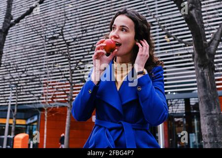 Donna d'affari in trench cappotto mangiare mela Foto Stock