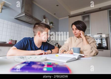 Madre e figlio si guardano mentre studiano dentro cucina a casa Foto Stock