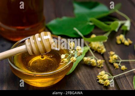 Bastone per miele in recipiente di vetro con miele di tiglio e fiori di tiglio freschi su un tavolo di legno. Messa a fuoco selettiva. Foto Stock