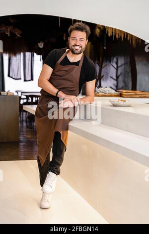 Bel cuoco maschile in grembiule seduto in un ristorante moderno Foto Stock