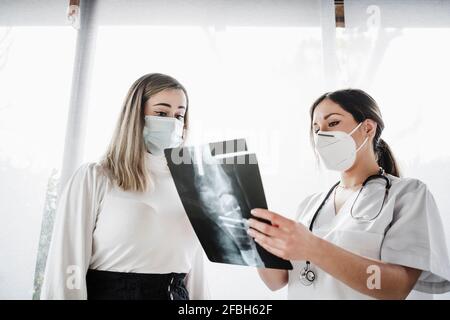 Medico di sesso femminile che mostra raggi X al paziente in clinica durante COVID-19 Foto Stock