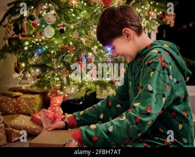 Ragazzo sorridente apertura confezione regalo da albero di Natale a casa Foto Stock