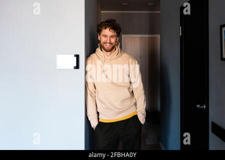 Uomo sorridente in piedi con le mani in tasca a casa Foto Stock