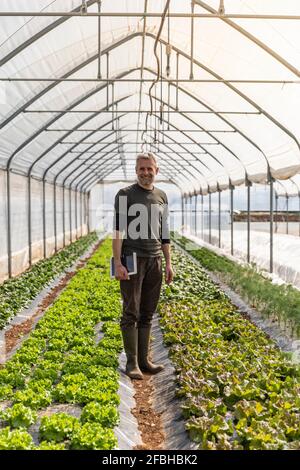 Agricoltore sorridente in piedi tra piante fresche a serra Foto Stock