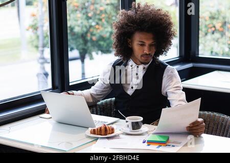 Giovane freelance che esamina i documenti mentre si siede a tavola nel caffè negozio Foto Stock