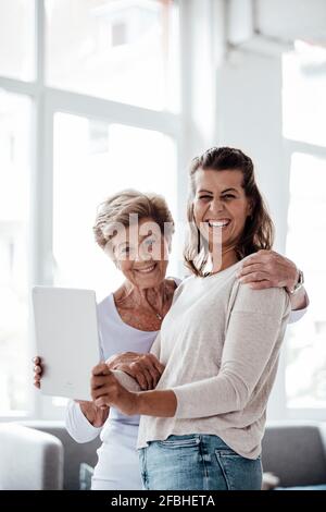 Giovane donna allegra che tiene il tablet digitale dalla nonna a casa Foto Stock