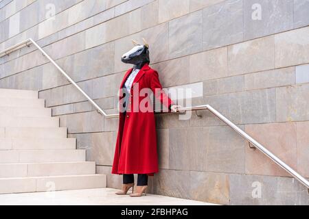 Donna che indossa il soprabito rosso e maschera di toro che tiene la ringhiera mentre in piedi vicino alla scala Foto Stock