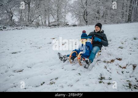 Il padre e il figlio giocosi dormono lungo la collina innevata durante l'inverno Foto Stock