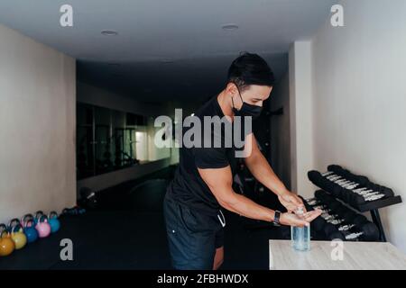 Persona sportiva che indossa una maschera protettiva per il viso utilizzando disinfettante per le mani in salute club Foto Stock