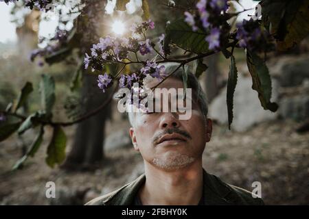 Uomo maturo con gli occhi chiusi ad albero fiorente in giardino Foto Stock