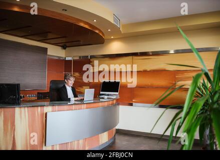 La receptionist sorridente usa un computer portatile alla reception dell'hotel Foto Stock