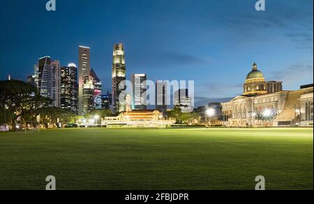 Singapore, Padang Field al crepuscolo con skyline illuminato della città sullo sfondo Foto Stock