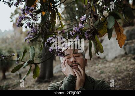 Uomo maturo con gli occhi chiusi sotto albero fiorente in giardino Foto Stock