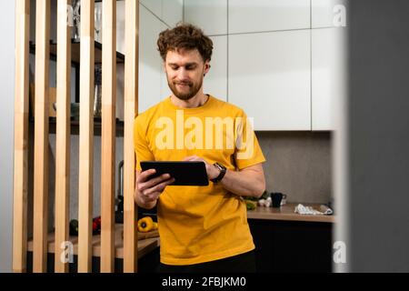 Bell'uomo che usa un tablet digitale mentre si trova in cucina domestica Foto Stock