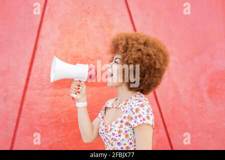 Donna rossa gridando sul megafono dalla parete rossa Foto Stock